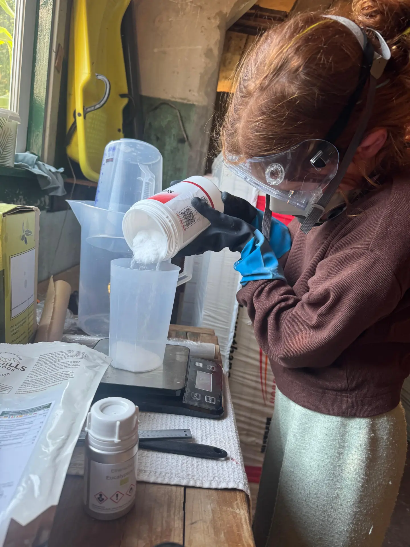 Madeline weegt met masker en handschoenen natriumhydroxide af op een weegschaal